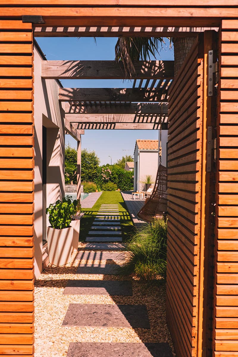 Aménagement de terrasse en bois avec claustra type persienne et porte d'accès au jardin par Rokaï Paysagiste